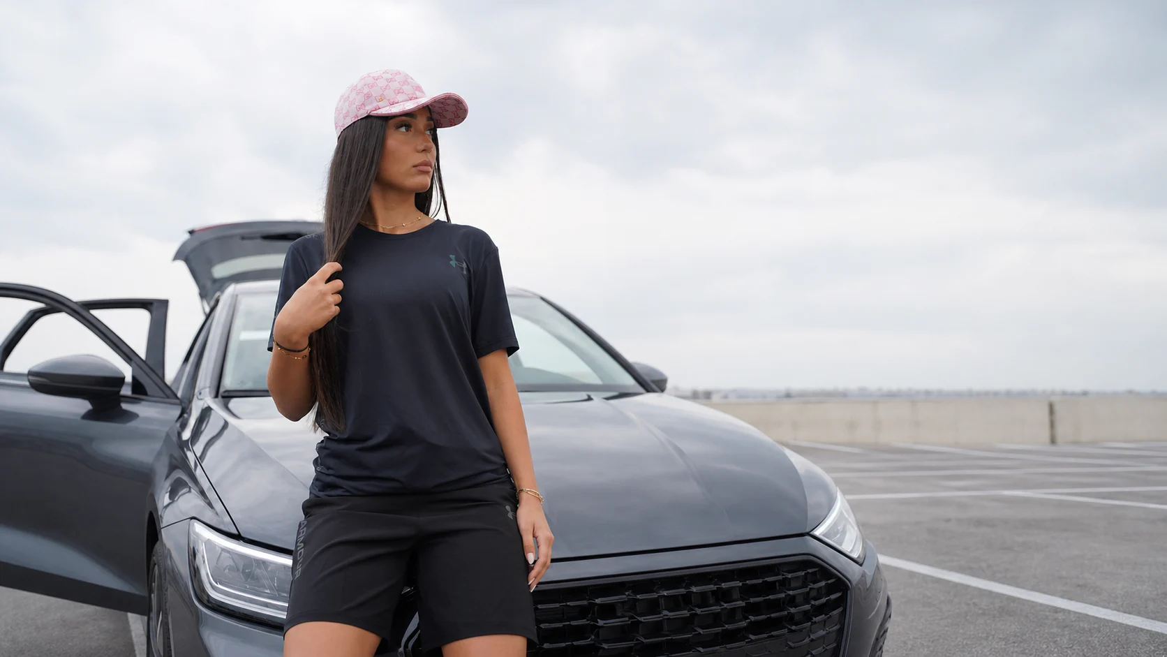 Modèle Under Gear portant un ensemble noir devant une Audi A3 sous un ciel clair